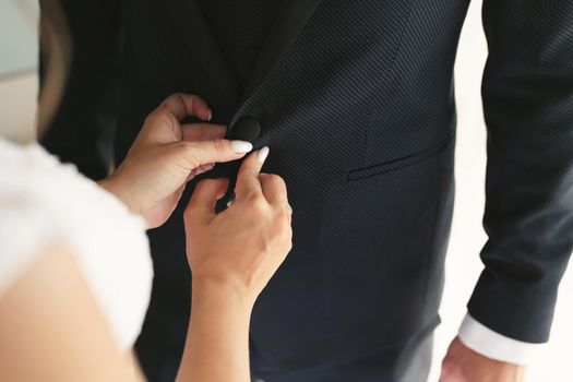 Bride helps the groom to button his jacket