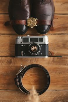 Wedding rings on an old camera, shoes, watch, and belt. Men's attributes on the wooden floor