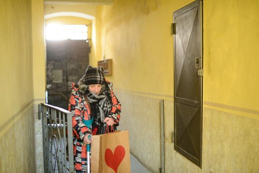 senior east european disabled woman entering a building with an architectural barrier opening a gate with one hand and holdding the crutch with the other also grabbing a bag dressed warm and shabby. High quality photo