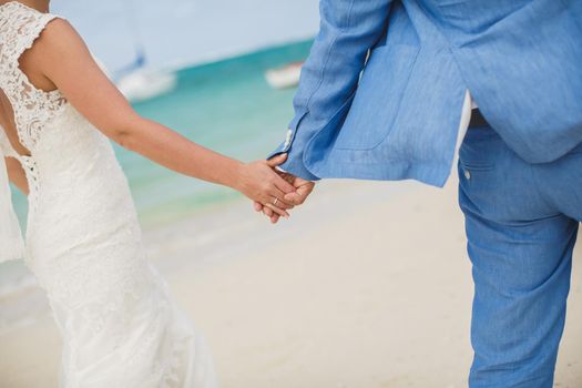 Beautiful gorgeous bride and stylish groom holding hands, on the background of a sea