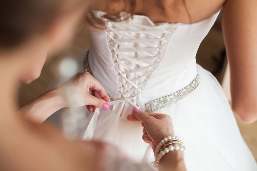 Bridesmaid makes bow-knot on the back of brides wedding dress