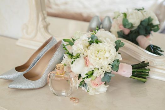 Silver shoes of the bride , perfume, bouquet and wedding rings on the dressing table near the mirror