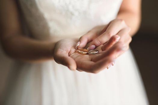 Bride in a white dress holds gold wedding rings in her hands