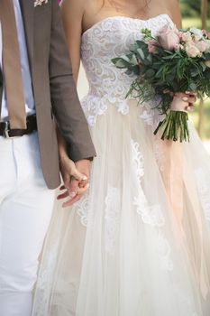 The bride and groom hold hands. The bride is holding a bouquet of flowers.