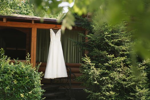 Beautiful wedding dress hangs on a wooden gazebo next to an outdoor Christmas tree