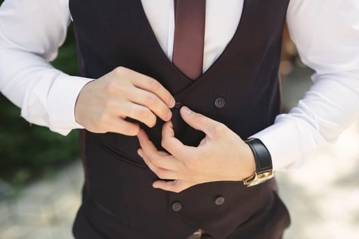 A man puts on a wedding suit and fastens a button.