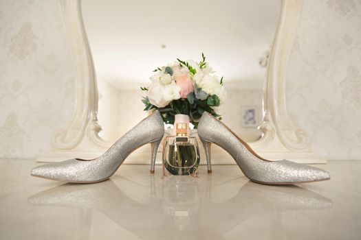 Silver shoes of the bride , perfume, bouquet and wedding rings on the dressing table near the mirror