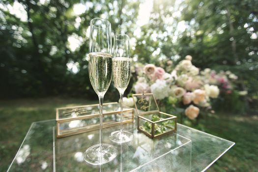 Gold wedding rings in a glass box, champagne glasses on a glass table
