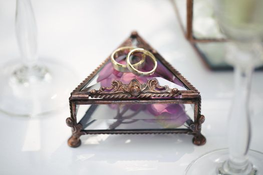 Wedding rings in a glass box with lilac rose petals