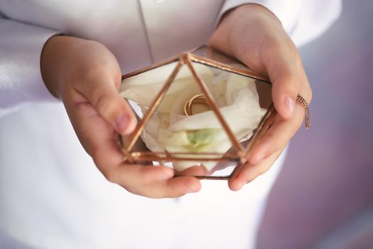 Gold wedding rings in a glass box with rose petals in women 's hands