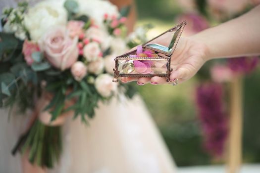 Gold wedding rings in a glass box with rose petals in women 's hands