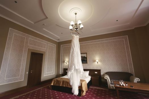 Luxurious white wedding dress hangs on hangers.