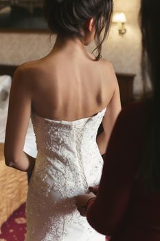 Female hands button the wedding dress to the bride with a beautiful hairstyle