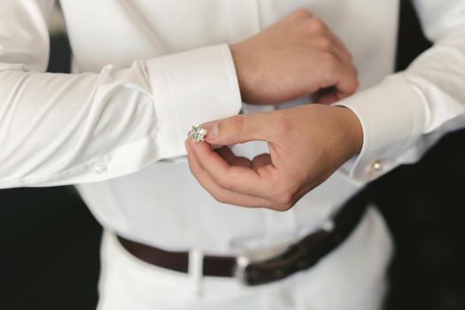 Men put on a shirt and fasten cufflinks on the morning of the wedding day.