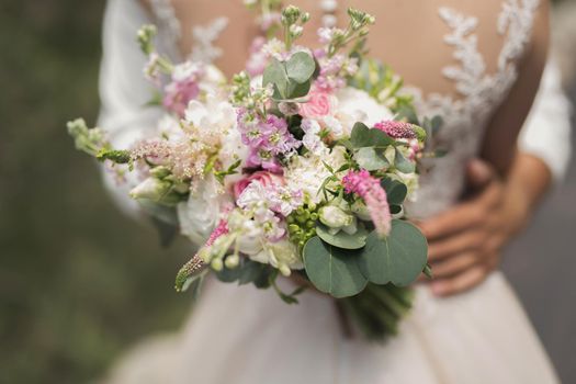 The groom in a white shirt with a bouquet of flowers in his hands embraces the bride.