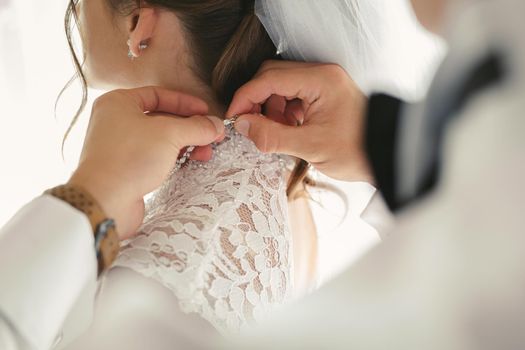 Female hands button the wedding dress to the bride with a beautiful hairstyle