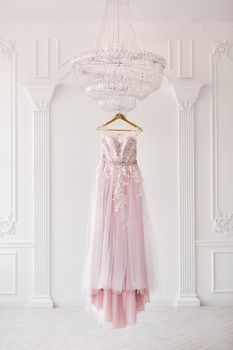 Rich pink wedding dress hangs on a chandelier in a white room