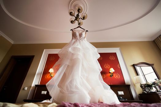 Luxurious white wedding dress hangs on hangers.