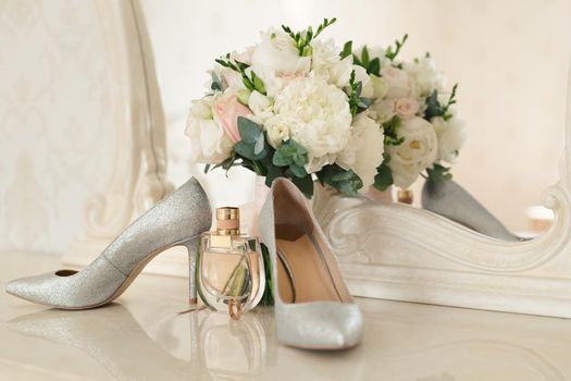Silver shoes of the bride , perfume, bouquet and wedding rings on the dressing table near the mirror