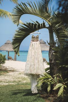 The wedding dress is hanging on a palm tree against the background of the ocean.