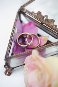 Wedding rings in a glass box with lilac rose petals