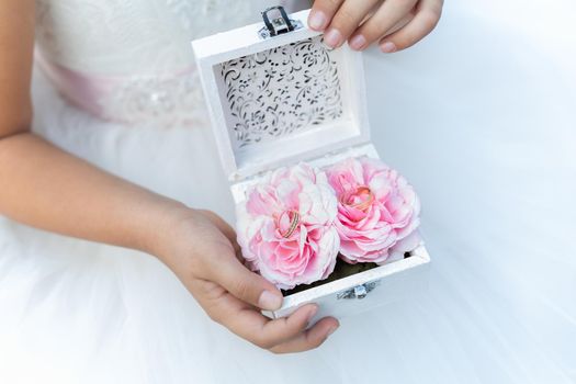 Woman hands holding glass casket with peony flower buds and wedding rings.