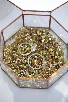 Glass box with wedding rings and gold sequins