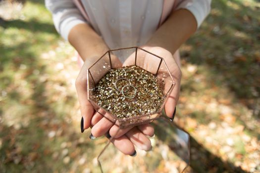 Glass box with wedding rings and gold sequins in women 's hands