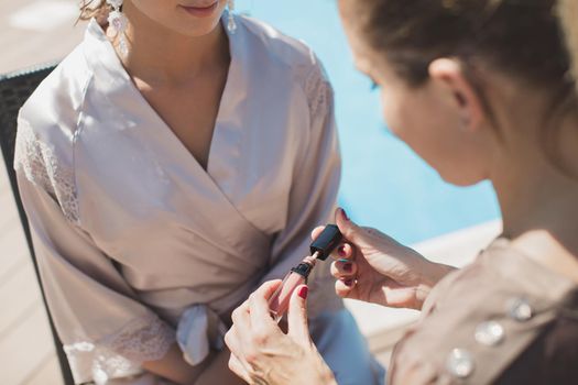 A young beautiful bride applying wedding makeup from a makeup artist. The morning training. Close-up of the hands next to the face