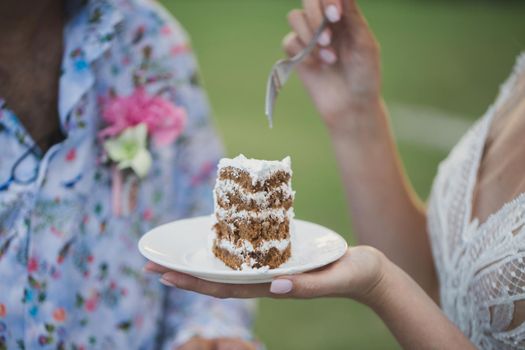 Beautiful young bride feeding wedding cake to groom outdoors