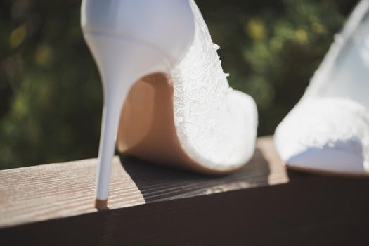 Elegant white wedding shoes on a wooden beam on the background of the pool.