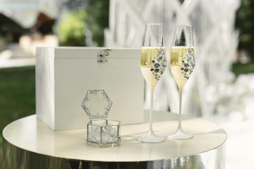 A box with wedding rings and gold sequins, champagne glasses, flowers.