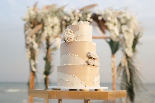 Wedding cake at a beach wedding on the background of a beautiful arch for an exit ceremony.