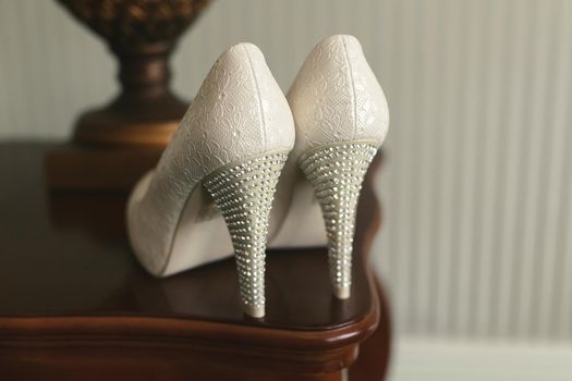 Wedding shoes with heels on a pedestal next to a table lamp.