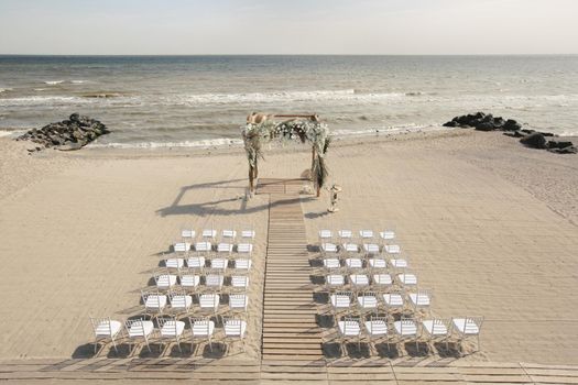 Outdoor area for beach ceremonies with sea view, white chairs, flower arch on a sunny day