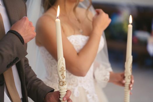 the wedding ceremony in the church. The bride in a white dress and veil holds candles.