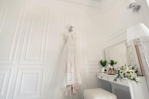 Elegant wedding white dress hanging on a wall during a wedding preparation. Bride's morning. Before ceremony