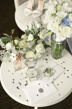 Bouquet with silk ribbons, female classic shoes, perfume bottle, necklace, earrings, wedding rings and shoes on vintage table.