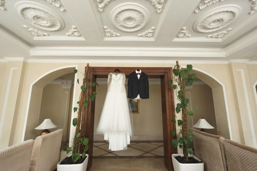 The bride's wedding dress and the groom's jacket on wooden hangers, hang on the wardrobe.