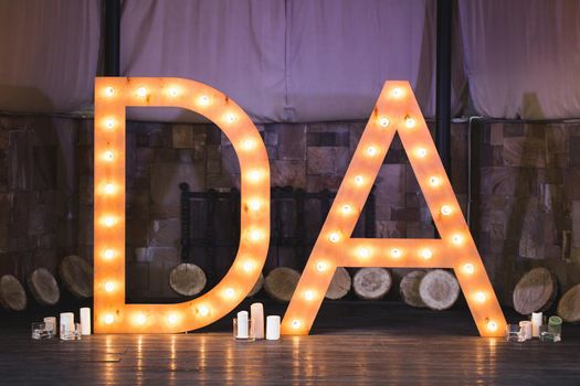 Wooden initials of the bride and groom with bright lights at the wedding.