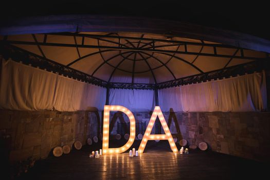 Wooden initials of the bride and groom with bright lights at the wedding.
