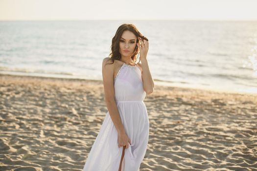Beautiful girl bride in a white dress and sneakers, at sunset walks along the beach.