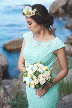 Bride in nature in the mountains near the water. Dress color Tiffany. Bride posing with bouquet.