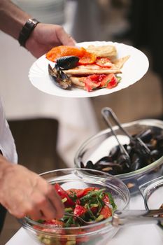 A man's hands put sea products on a plate at a buffet.