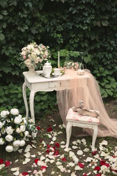 Romantic photo zone for the bride's wedding day gatherings. Table, flowers and rose petals in the forest.
