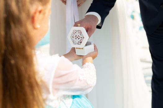 A little girl keeps wedding rings in a small box. Outdoor wedding ceremony