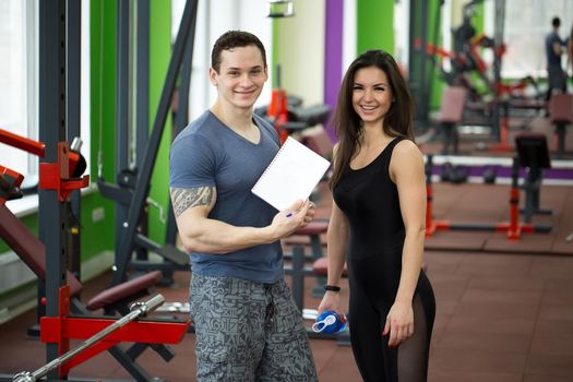 Handsome muscled male trainer consulting attractive young female in gym, both smiling