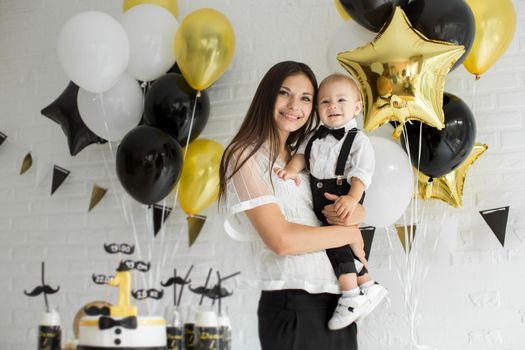 Mother and son celebrating the 1st birthday together laughing and smiling with balloons, a candy bar.
