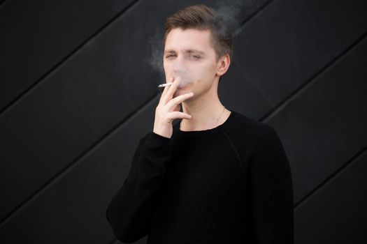 Young handsome guy Smoking a cigarette on black background