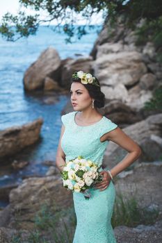 Bride in nature in the mountains near the water. Dress color Tiffany. Bride posing with bouquet.